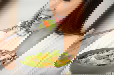 Lady eating a caesar salad with lettuce, egg, and tomato 
