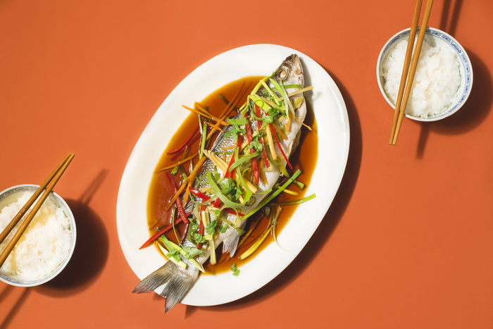 Cantonese-Style Recipes for Chinese New Year festive table. Sea bass or Spigola fish steamed with ginger, red peppers in soy sauce served white rice. Steamed fish - a symbol of prosperity and wellness in China
