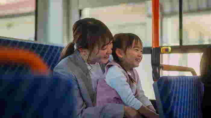 An Asian businesswoman is commuting by bus with her small daughter.