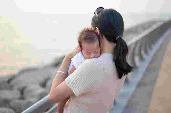 Cute young mother is holding her sleeping newborn baby boy in her arms. A woman enjoying in motherhood and spending time with her baby in the fresh, summer, sea air